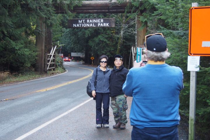 people posing for the camera in front of mt rainier national park sign