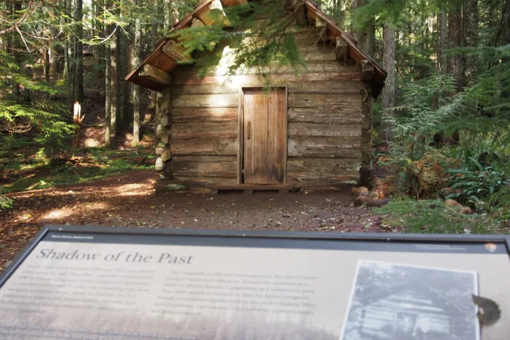 A historical sign with a wood cabin behind on a mt rainier tour