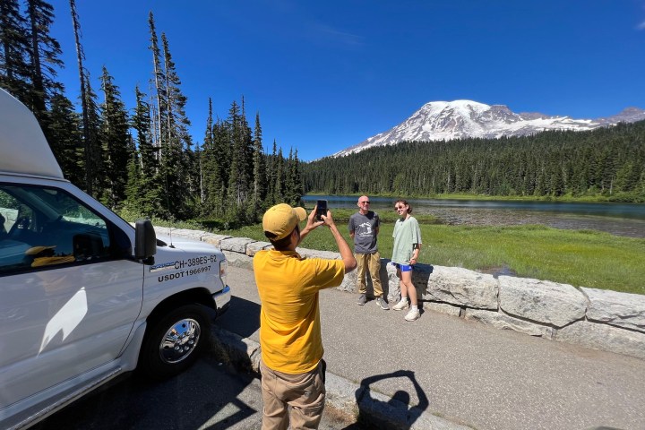 person taking a photo of people in front of trees and Mt. Rainier during a Tours Northwest guided tour