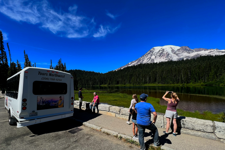 people taking pictures of a lake with trees and a mountain