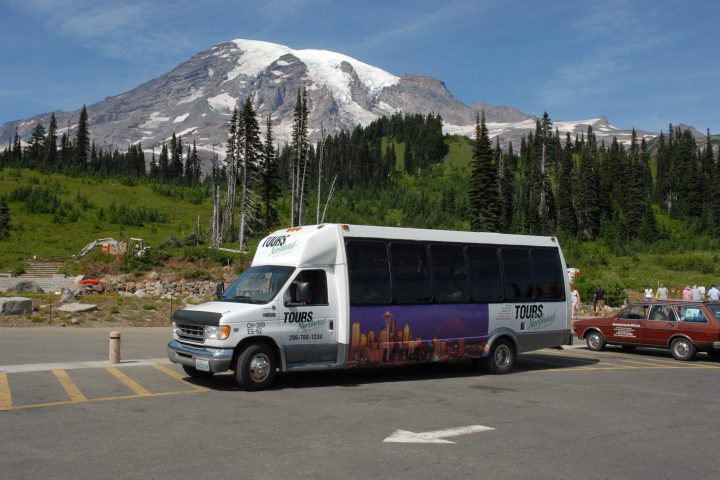 a Pacific Northwest tour bus in parking lot with mountain in background on a mt rainier tour