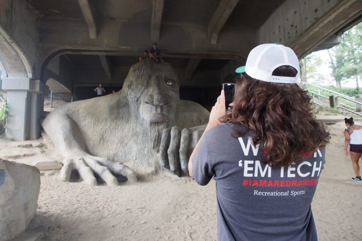 person taking a photo of people on Fremont Troll under bridge