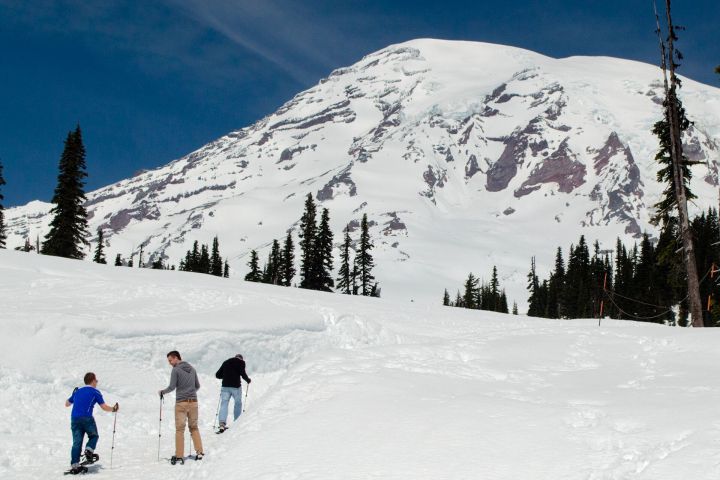 Three people snowshoeing up a snowy slope with a mountain backdrop.