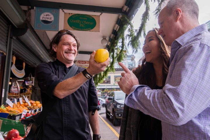 a man and woman standing in front of a fruit stand during a seattle excursion
