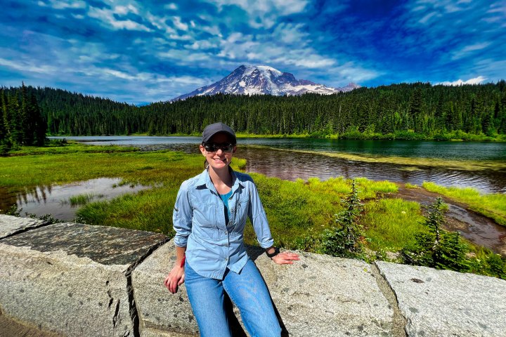 person on a rock with Mt Rainier in the background as seen on a day tour from Seattle