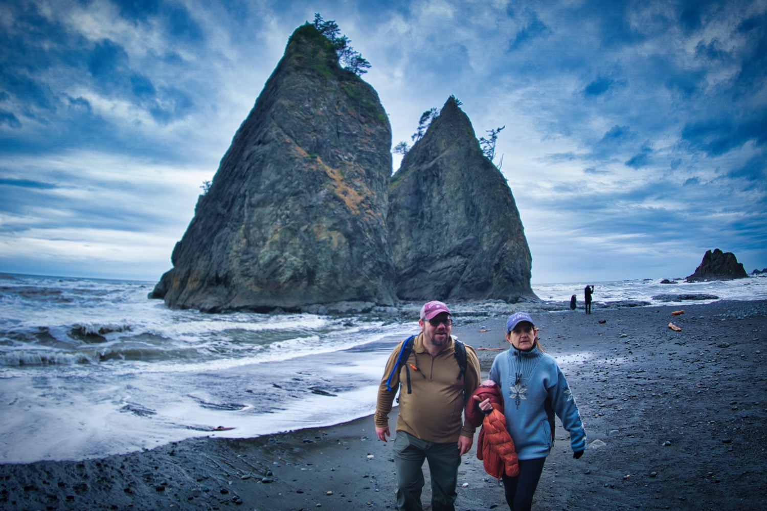 a man and a woman standing in front of a sea stack at Rialto Beach on an Olympic National Park Tour