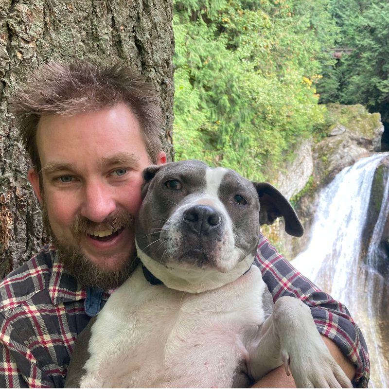a tours northwest tour guide and his dog with trees and a waterfall in the background