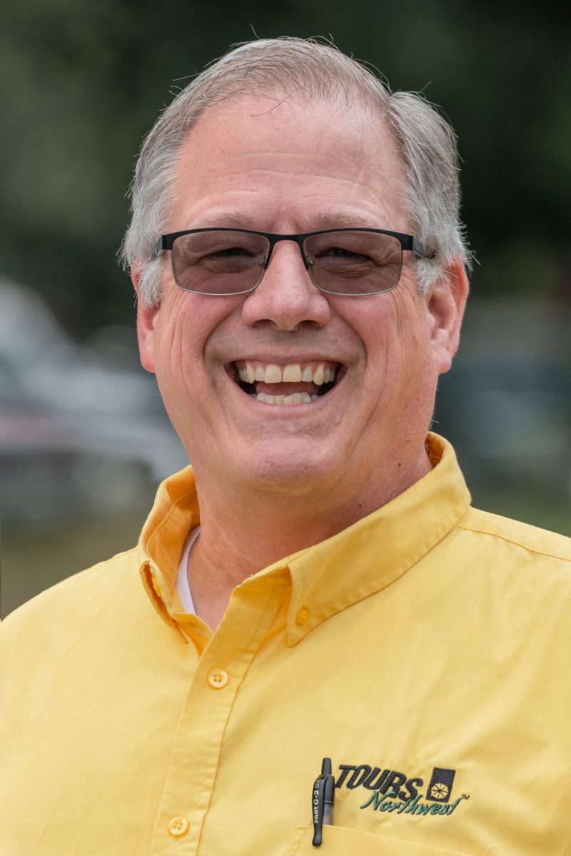 a tours northwest tour guide wearing glasses and a yellow shirt and smiling at the camera