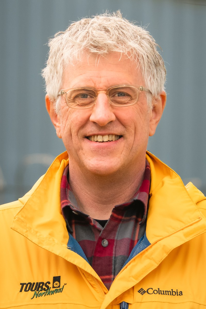 a tours northwest tour guide wearing glasses and a yellow jacket and smiling at the camera