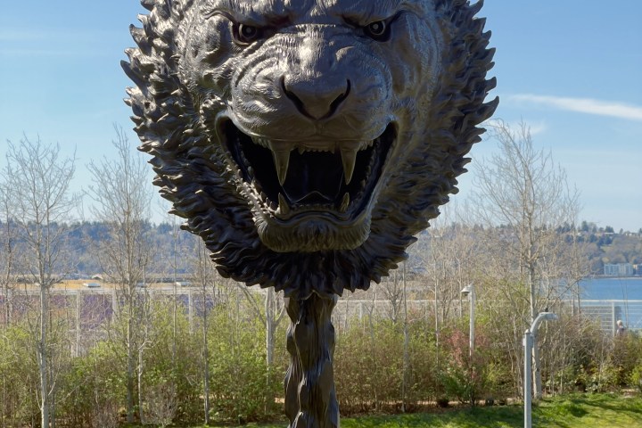 Statue of a roaring tiger head on a pole in a park setting.