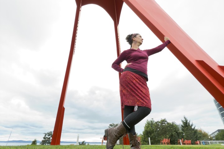 Person in red outfit leaning on large red sculpture in a grassy field.