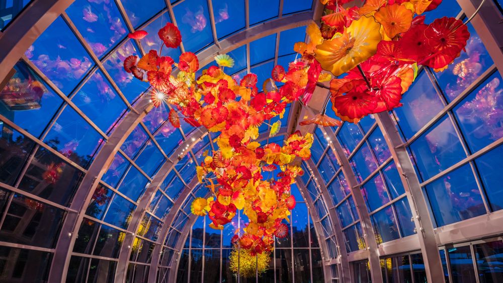 Glass ceiling with vibrant red and yellow glass flowers against deep blue sky.