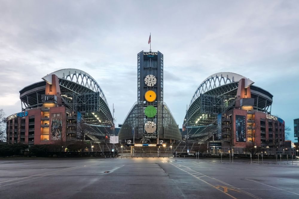 Exterior view of Lumen Field, a large stadium with arching roofs and a central tower.