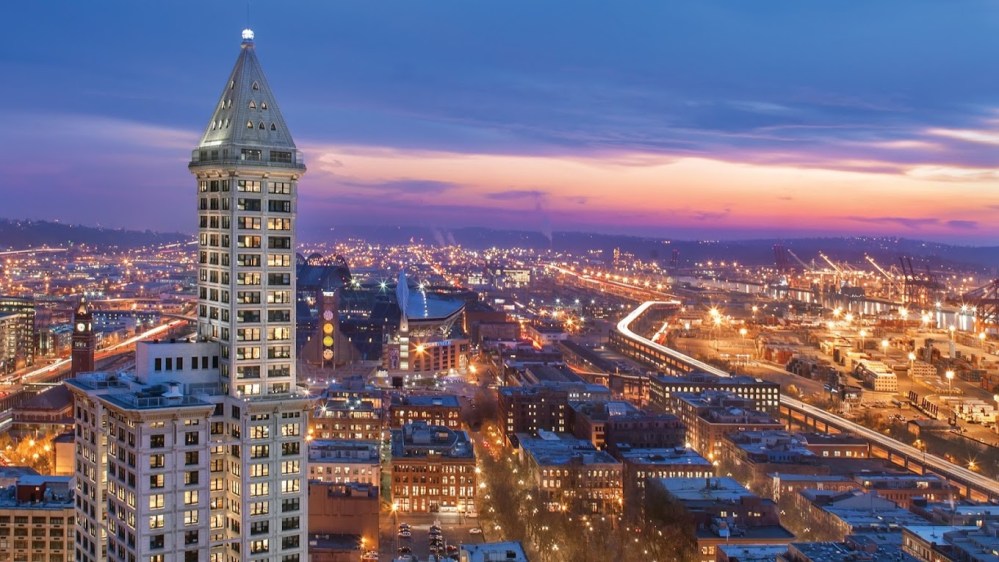 City skyline at dusk with tall building and lit streets.