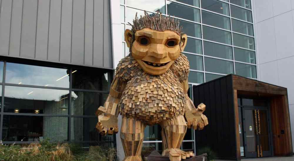 Large wooden troll sculpture in front of a modern building with glass facade.