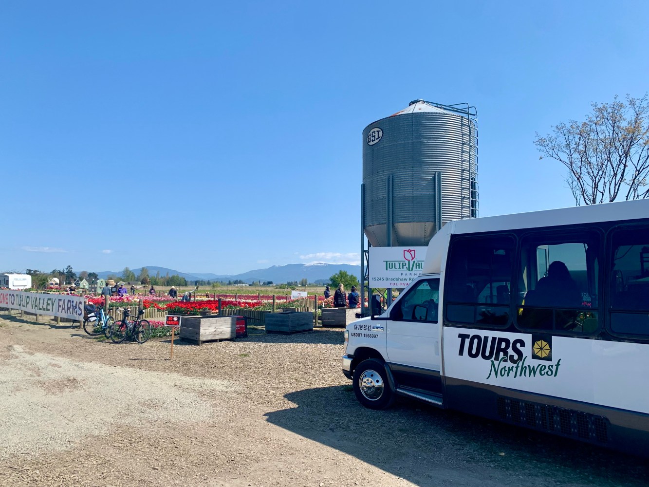 Tour bus at Tulip Valley Farms entrance with silo and tulip fields in the background.