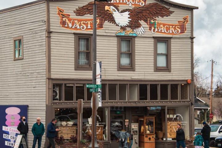 Street view of an antique shop with an eagle mural, people walking by on a cloudy day.