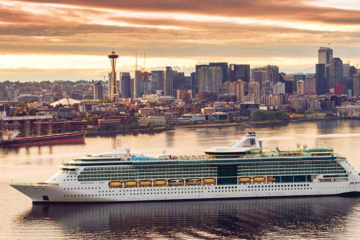 Cruise ship sailing with Seattle skyline, including the Space Needle, during sunset.