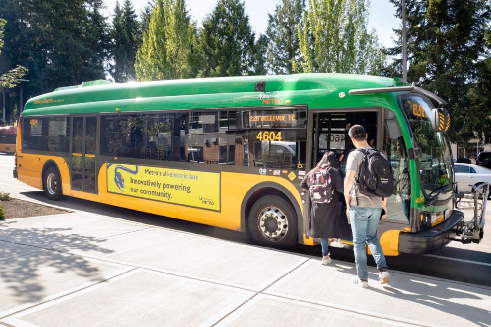 Two people board a green and yellow bus at a station.