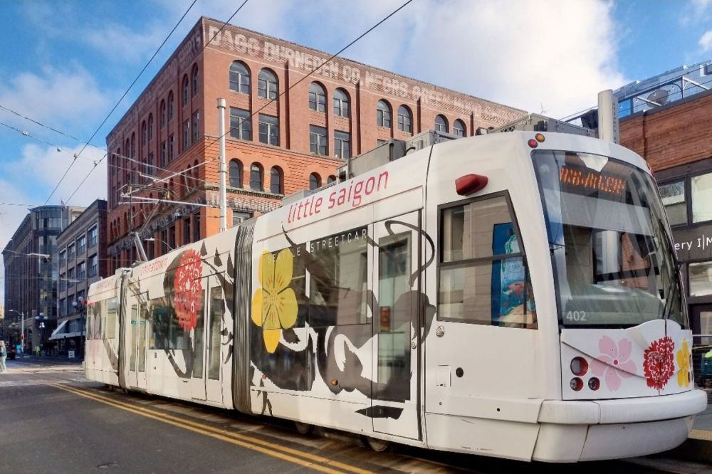 White tram with floral design on urban street near brick building.
