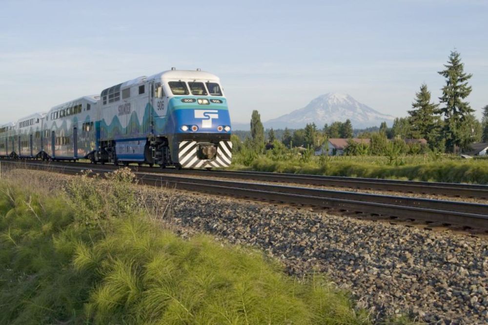 Passenger train on tracks with mountain and houses in background.