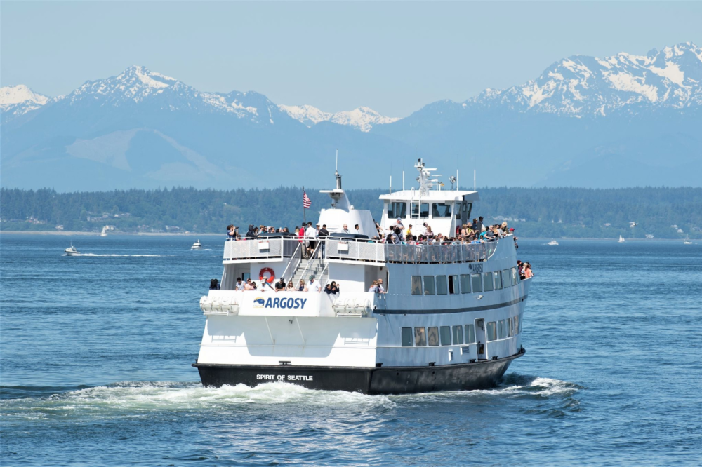 Ferry with passengers on a sunny day, mountains in the background.